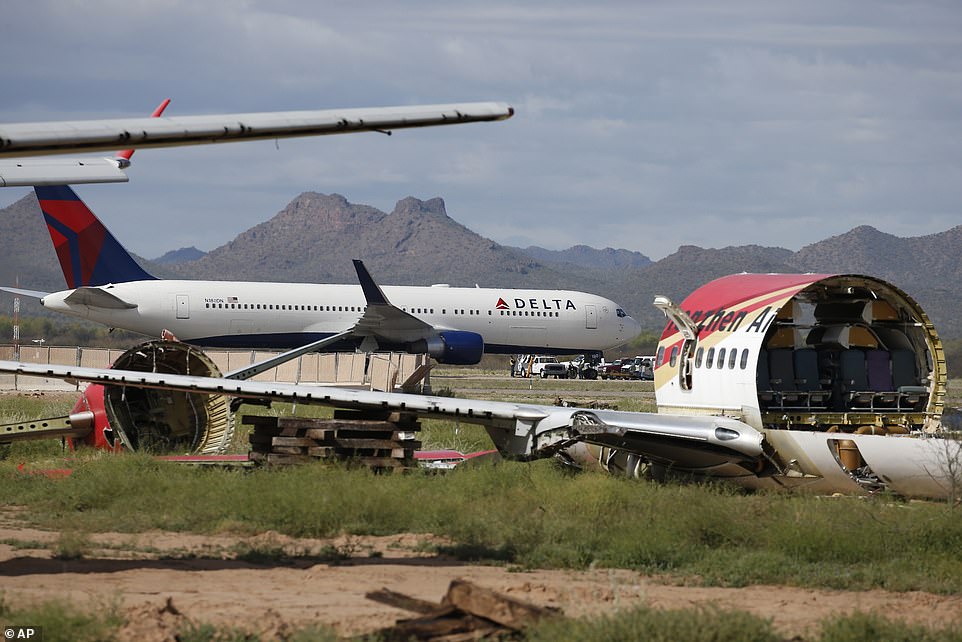 With a stripped passenger plane in the foreground, a recently landed Delta Air Lines airplane is worked on by ground crew