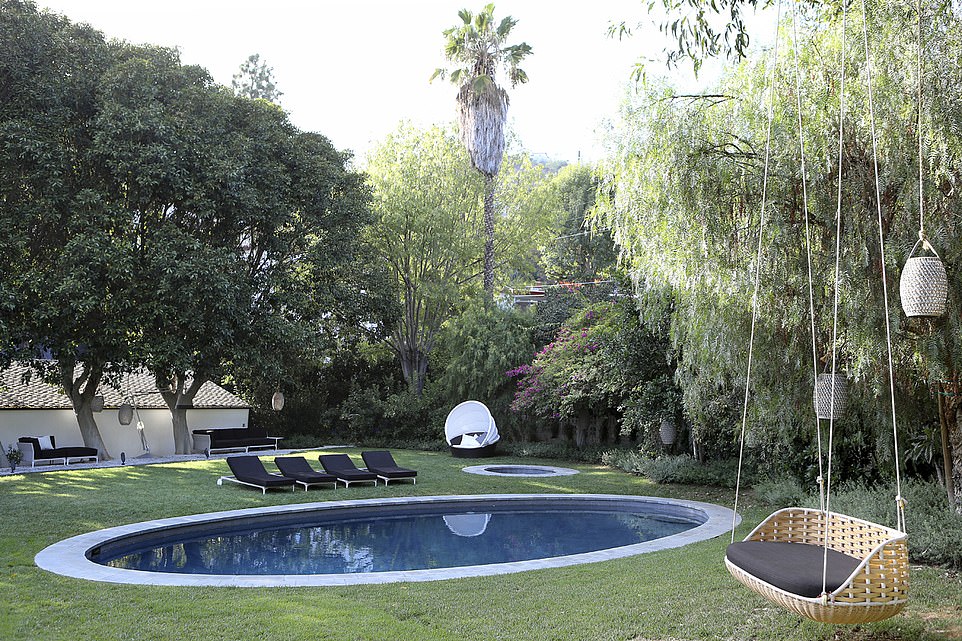 The grounds incorporate a variety of eye-catching tiled terraces, an outdoor kitchen and a stunning, oval-shape swimming pool (pictured) which is made private thanks to a wall of dense foliage