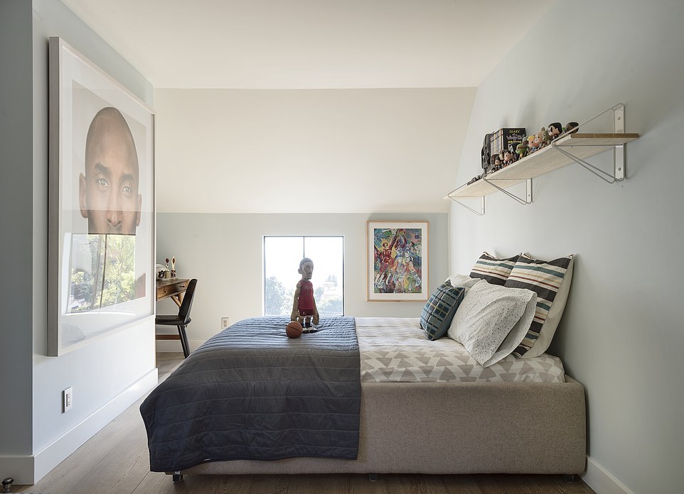 A stunning room decorated for a youngster. It features sporty artwork, a sturdy shelf and stylish bedding along with white and light blue painted walls