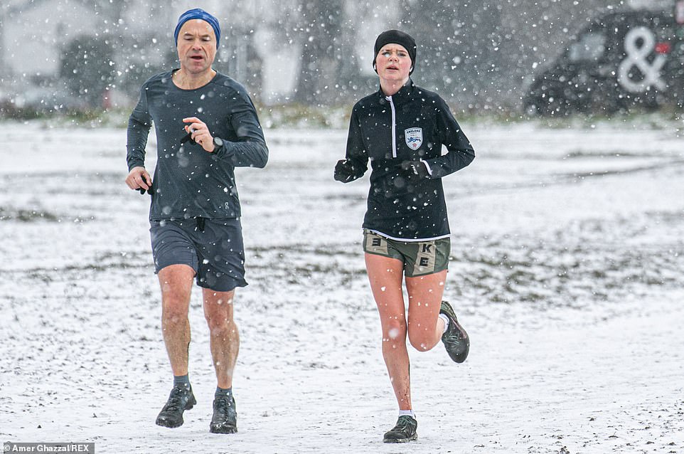 People jogging during a snow shower on Wimbledon Common this morning in Wimbledon, London