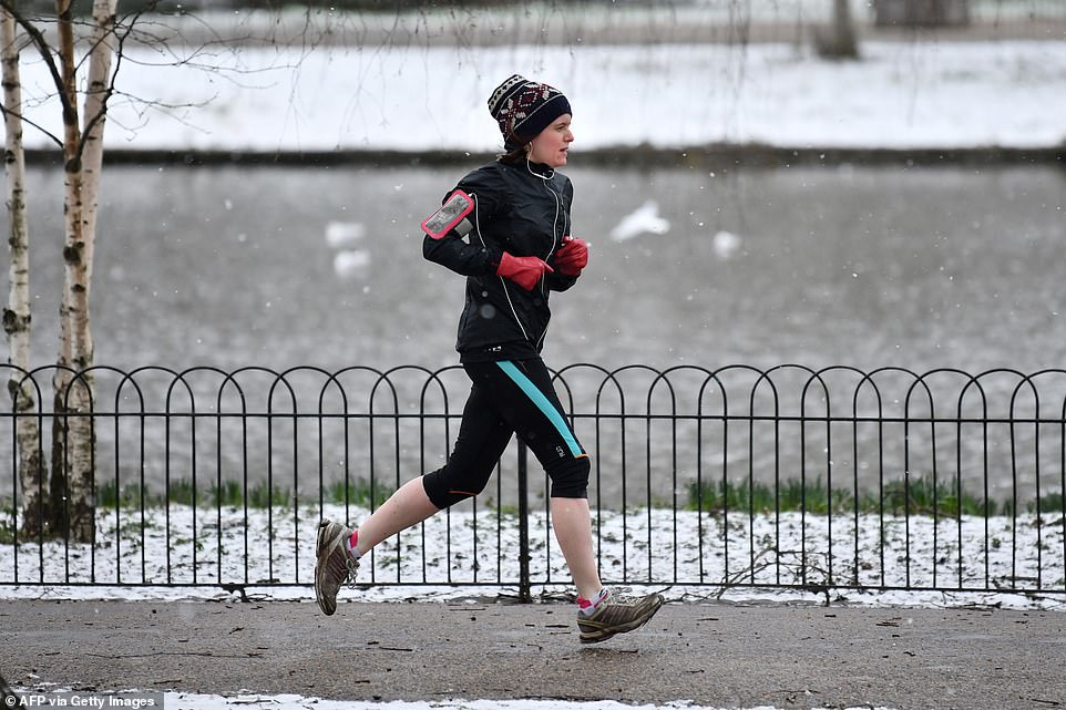 A hardy jogger runs through a snow-covered Green Park in central London this afternoon