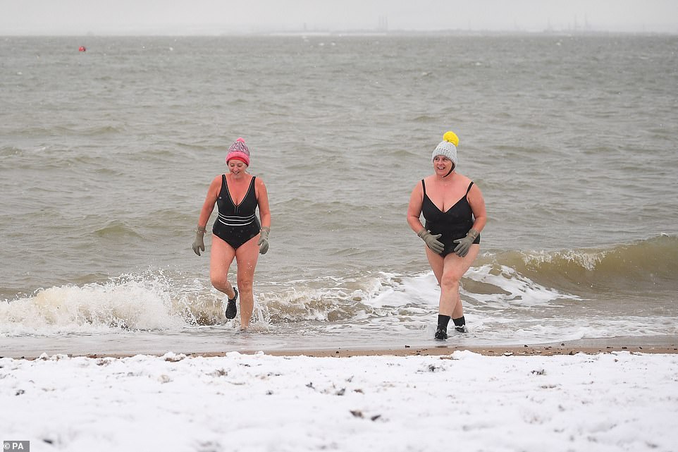 Early morning swimmers were seen jumping into the sea in just swimsuits and swimming caps while snow covered the beach