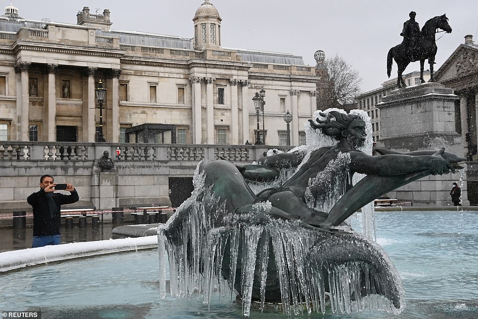 A man takes a photo of the fountain covered in icicles at Trafalgar Square, as Storm Darcy affects large parts of the country