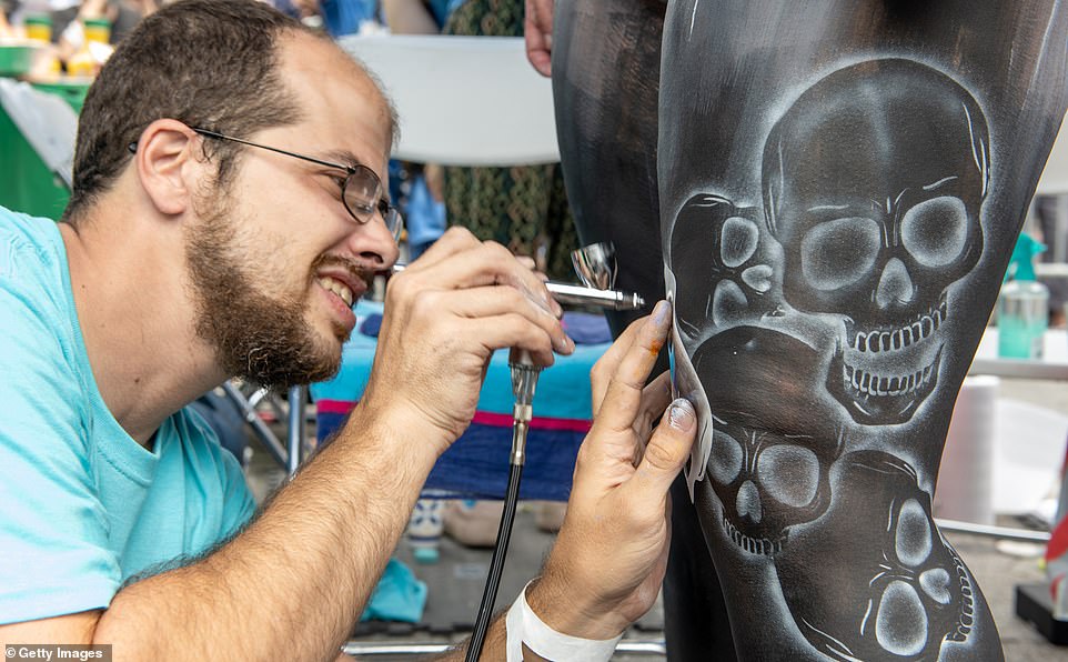 An artist spray paints skulls on a model's leg during in theBody Painting Day