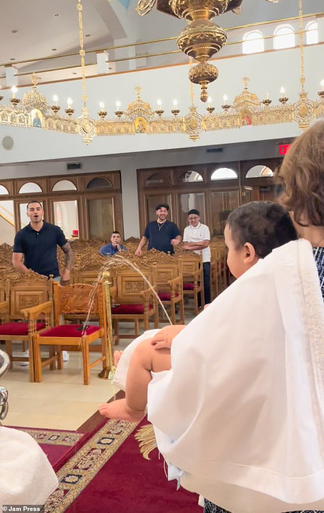 Members of the congregation can be seen bursting into peels of laughter as the baby's stream of urine makes a large upward arc