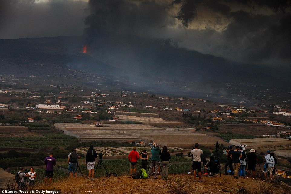People watch the erupting volcano from a nearby vantage point, as police warn that tourists should stay well away in case they hamper evacuation efforts or get too close to the lava