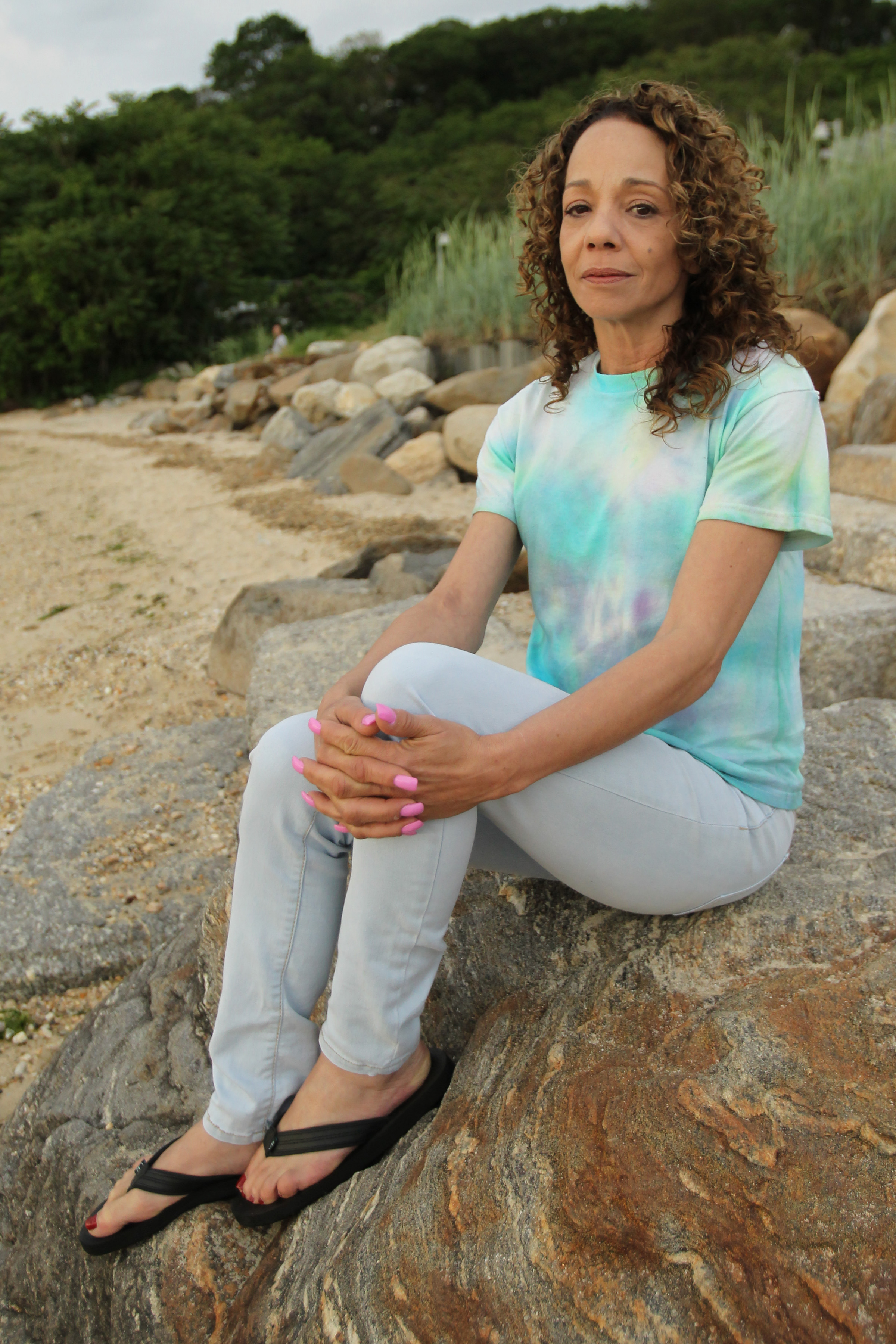 Mariah Carey's sister Alison Carey wearing a tie-dye shirt, skinny jeans, and flip flops during a photoshoot with The Sun